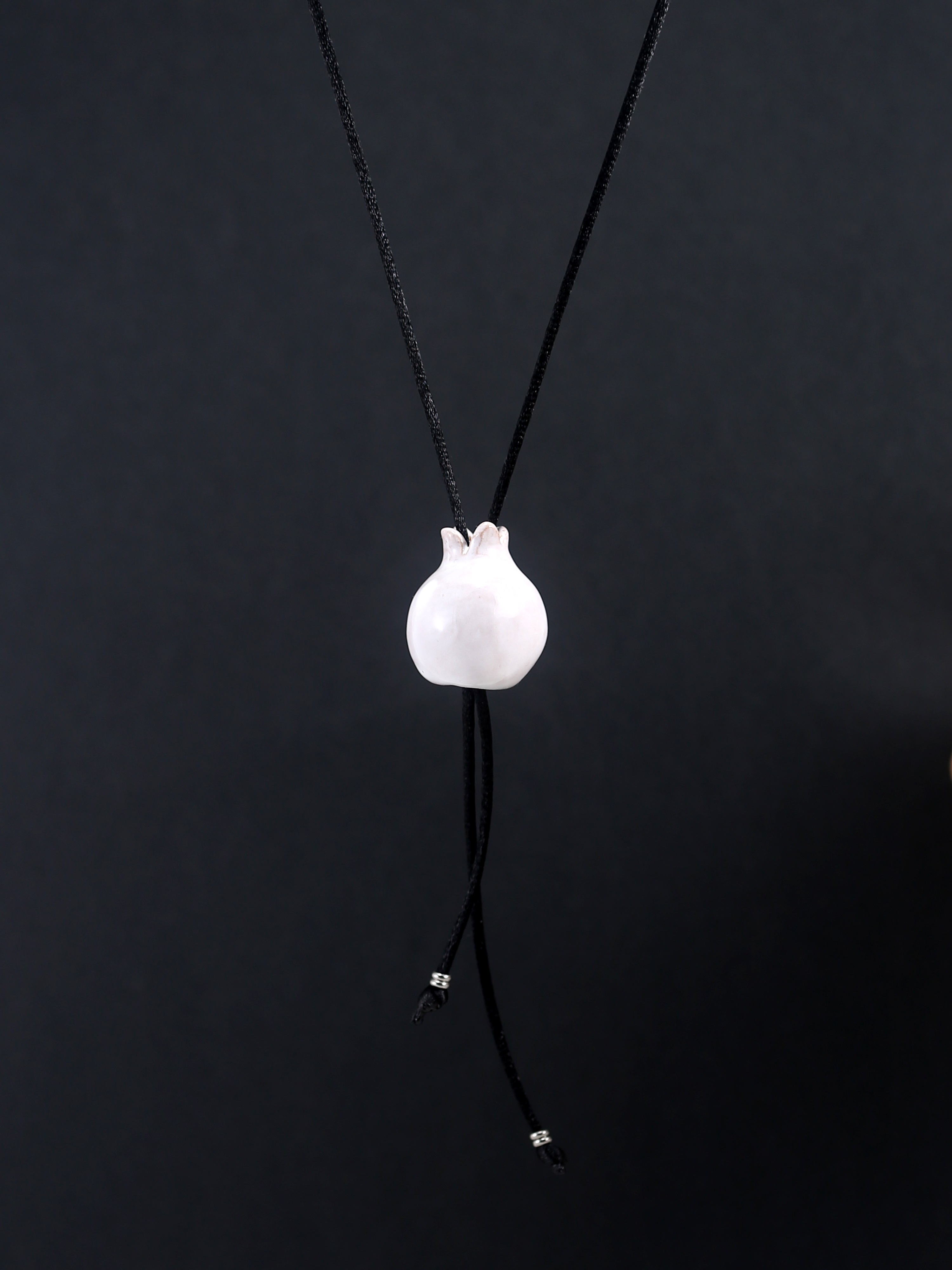 Immagine di Mini melagrana gioiello portafortuna collana artigianale ceramica bianca su sfondo nero.