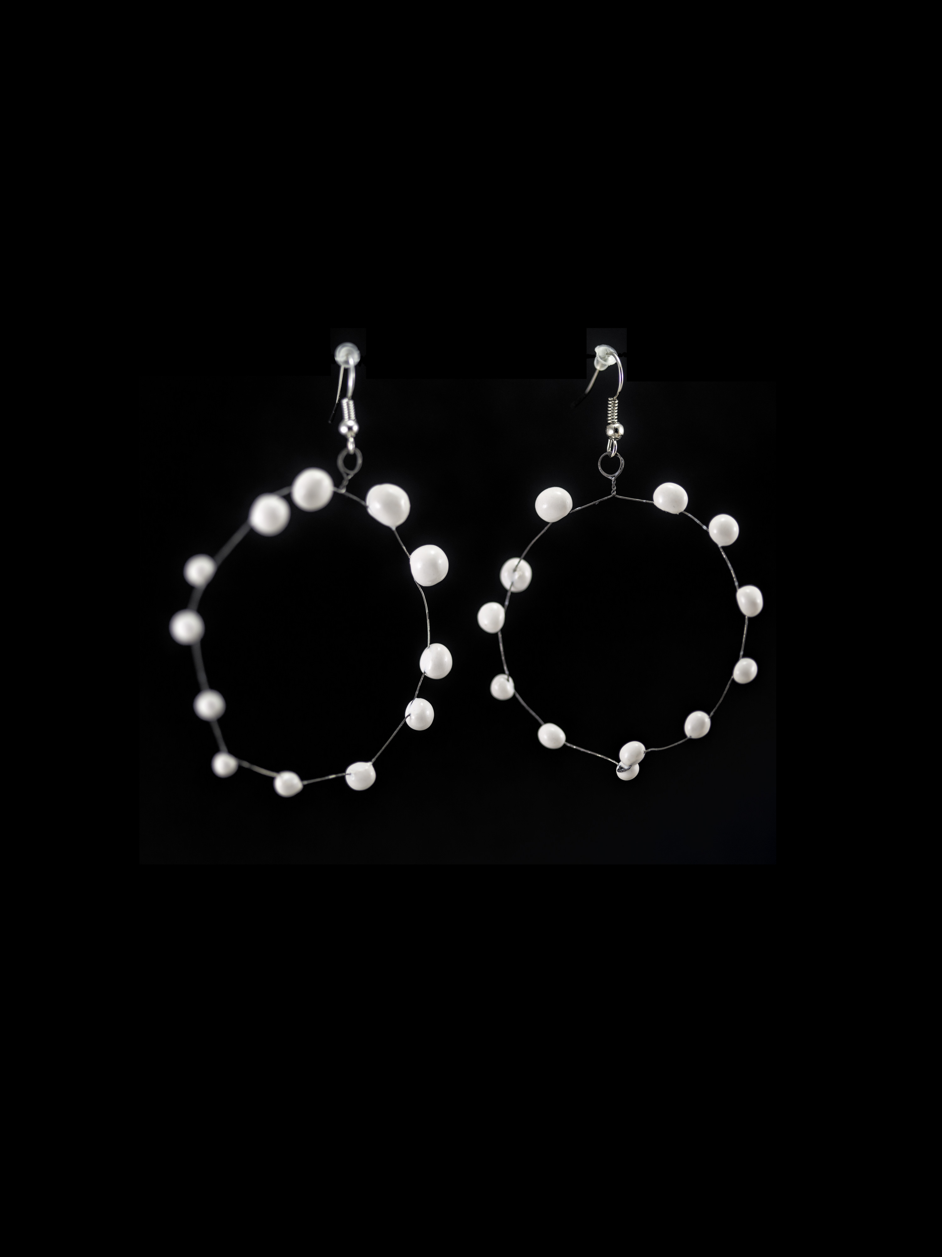 Coppia di orecchini a cerchio in ceramica e metallo, leggerissimi. Colore bianco su sfondo nero.
